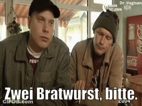 Two Men Are Sitting At A Table With A Coca Cola Fridge In The Background GIF
