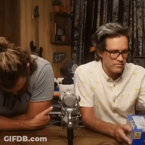 Two Men Are Sitting At A Table With A Microphone And A Box Of Cheerios GIF