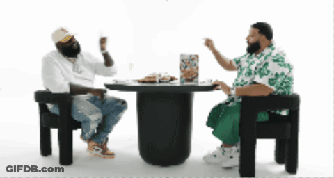 Two Men Are Sitting At A Table With A Pizza On It GIF