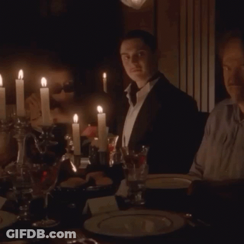 Two Men Are Sitting At A Table With Candles Lit GIF