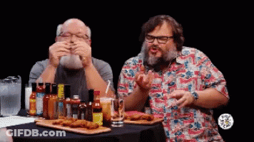 Two Men Are Sitting At A Table With Hot Sauce Bottles GIF