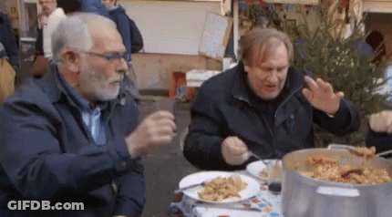 Two Men Are Sitting At A Table With Plates Of Food GIF