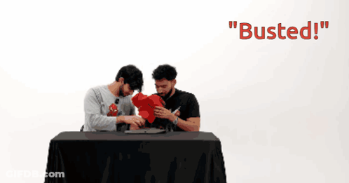 Two Men Are Sitting At A Table With The Words " Busted " On The Bottom GIF