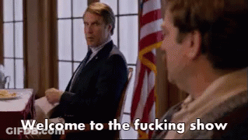 Two Men Are Sitting At A Table With The Words Welcome To The Fucking Show Written On The Screen . GIF