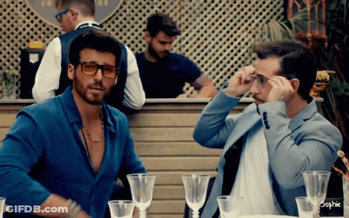 Two Men Are Sitting At A Table With Wine Glasses And The Word Sophie On The Bottom GIF