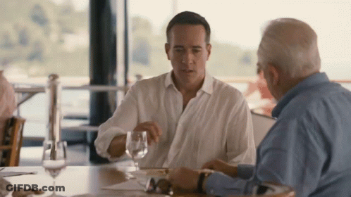Two Men Are Sitting At A Table With Wine Glasses GIF