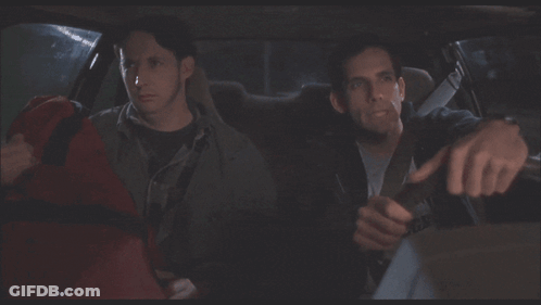 Two Men Are Sitting In A Car And One Of Them Is Holding A Red Bag GIF