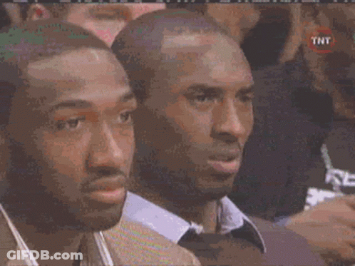 Two Men Are Sitting In A Crowd Watching A Basketball Game And One Of Them Has A Tnt Logo On His Shirt . GIF