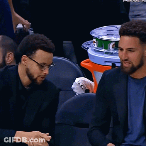 Two Men Are Sitting In A Stadium With A Gatorade Cooler In The Back GIF