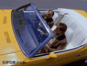 Two Men Are Sitting In A Yellow Convertible With The Roof Up GIF