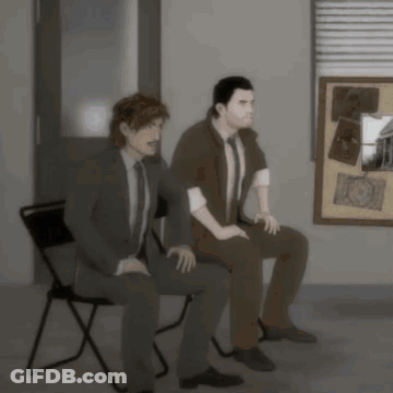 Two Men Sitting In Front Of Bulletin Board GIF