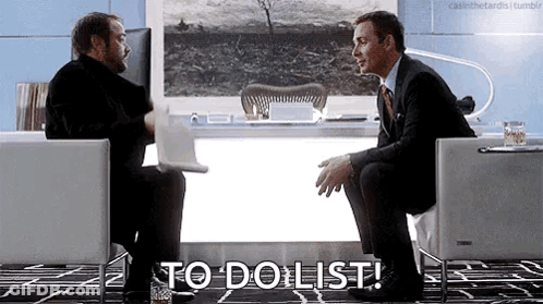 Two Men Are Sitting In Chairs In Front Of A Desk Talking To Each Other And One Of Them Is Holding A Laptop . GIF