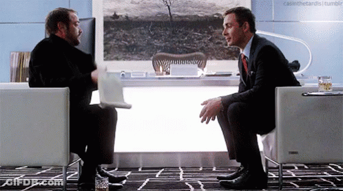 Two Men Are Sitting In Chairs Talking To Each Other GIF