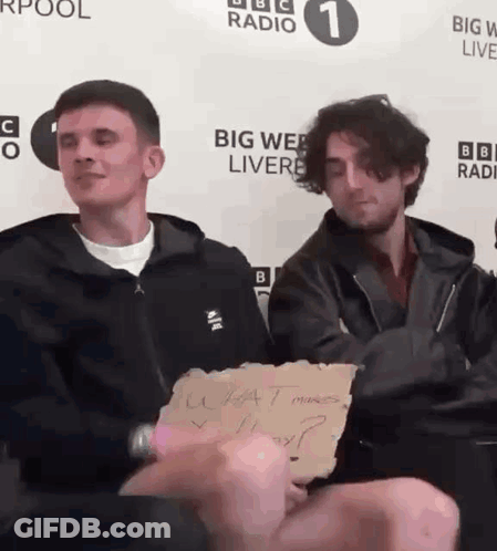 Two Men Are Sitting In Front Of A Big Web Live Sign GIF
