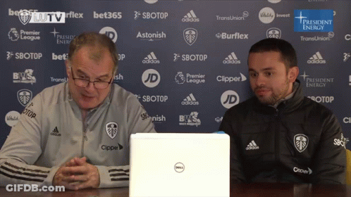 Two Men Are Sitting In Front Of A Dell Laptop In Front Of A Blue Backdrop GIF