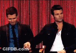 Two Men Are Sitting In Front Of A Red Curtain Holding Hands GIF