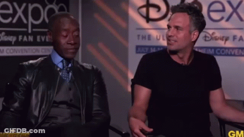 Two Men Are Sitting In Front Of A Sign That Says Disney Fan Expo GIF