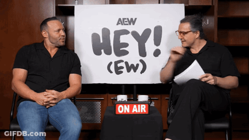 Two Men Are Sitting In Front Of A Sign That Says Hey ( Ew ) GIF