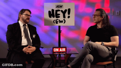 Two Men Are Sitting In Front Of A Sign That Says Hey ( Ew ) GIF