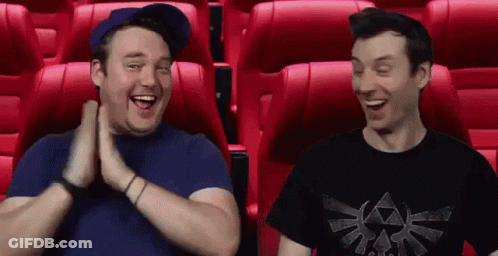 Two Men Are Sitting In Red Seats In A Movie Theater And Laughing . GIF