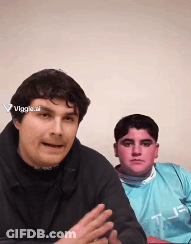 Two Men Are Sitting Next To Each Other And One Has A Viggle.ai Sticker On His Head GIF