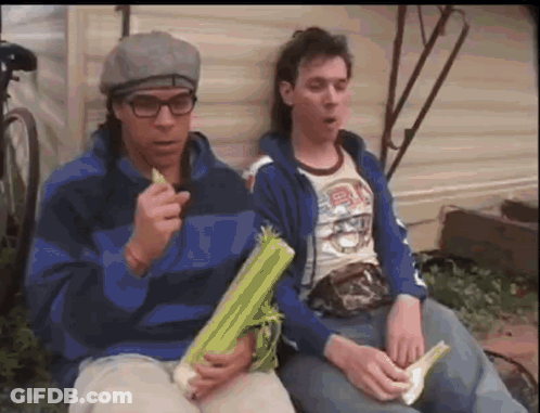 Two Men Are Sitting Next To Each Other And One Of Them Is Holding A Piece Of Celery GIF