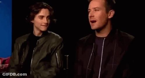 Two Men Are Sitting Next To Each Other In A Dark Room And Talking To Each Other . GIF