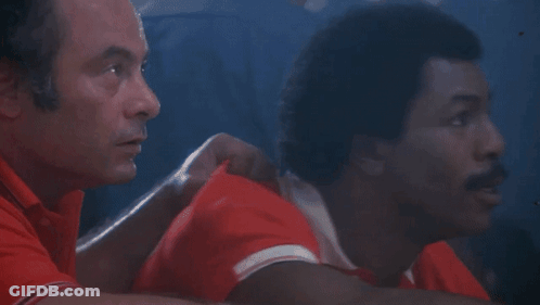 Two Men Are Sitting Next To Each Other In A Dark Room . GIF