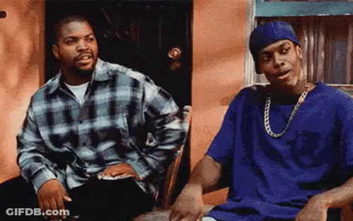 Two Men Are Sitting Next To Each Other In Front Of A Building . GIF