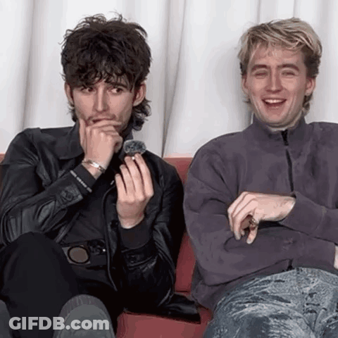 Two Men Are Sitting Next To Each Other On A Couch And One Is Holding A Ring In His Hand . GIF