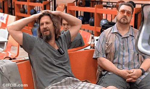 Two Men Are Sitting On A Bench In A Bowling Alley With Their Hands On Their Heads . GIF