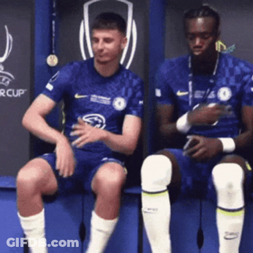 Two Men Are Sitting On A Bench In A Locker Room . GIF