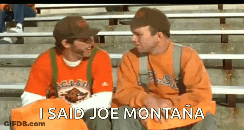 Two Men Are Sitting On A Bleacher Talking To Each Other And One Of Them Is Wearing An Orange Shirt . GIF