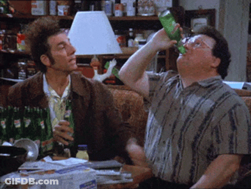 Two Men Are Sitting On A Couch Drinking Soda From Green Bottles GIF