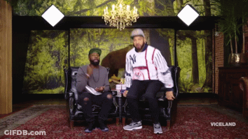 Two Men Are Sitting On A Couch In Front Of A Wall With Trees And The Word Viceland On It GIF