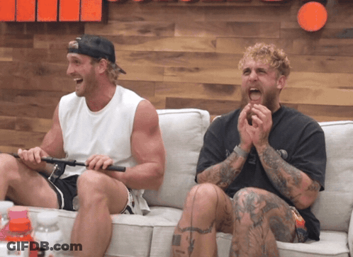 Two Men Are Sitting On A Couch Laughing And One Has A Tattoo On His Leg GIF