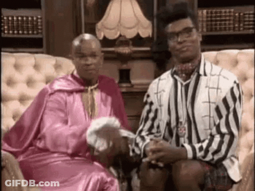 Two Men Are Sitting On A Couch With A Lamp In The Background . One Of The Men Is Wearing A Pink Robe . GIF