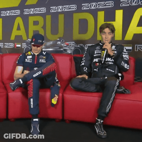 Two Men Sitting On Red Couch In Front Of Tabu Dha Sign GIF