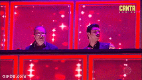 Two Men Are Sitting On A Stage In Front Of A Pink Background . GIF