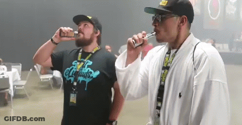 Two Men Are Smoking Electronic Cigarettes And One Has A Shirt That Says E Liquids On It GIF