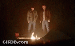Two Men Are Standing Around A Fire In The Dark . GIF