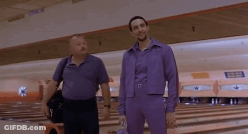 Two Men Are Standing In A Bowling Alley Wearing Purple Jumpsuits . GIF