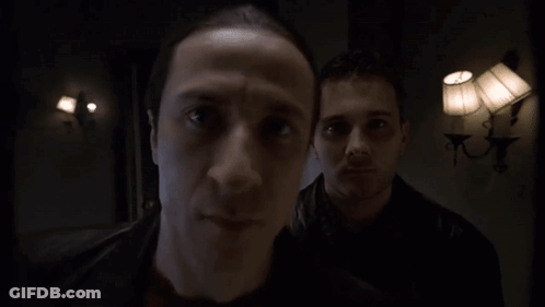 Two Men Are Standing In A Dark Room With Lamps On The Wall GIF