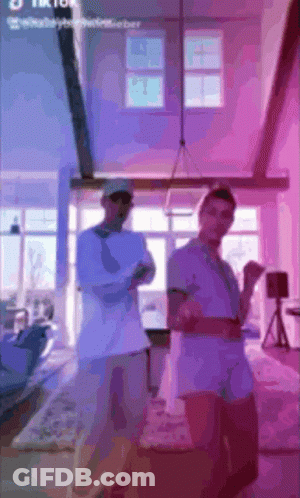 Two Men Are Standing In A Living Room With Purple Lights Behind Them And The Words Tik Tok On The Bottom GIF