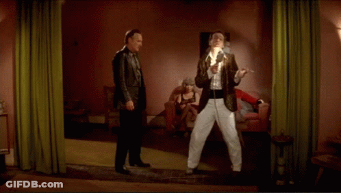 Two Men Are Standing In A Room With A Woman Sitting In A Chair GIF