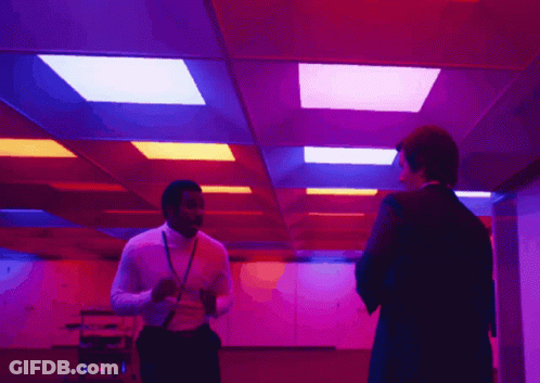 Two Men Are Standing In A Room With Purple And Red Lights On The Ceiling GIF