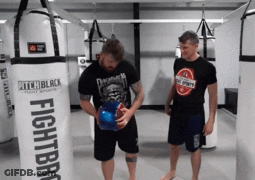 Two Men Are Standing In Front Of A Boxing Bag That Says Pitch Black GIF