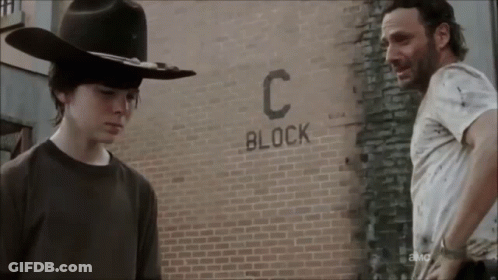 Two Men Are Standing In Front Of A Brick Wall That Says Block C. GIF