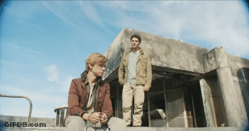 Two Men Are Standing In Front Of A Building With A Blue Sky Behind Them GIF