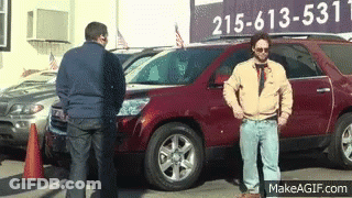 Two Men Are Standing In Front Of A Car Dealership With A Sign That Says 215-613-5331 GIF